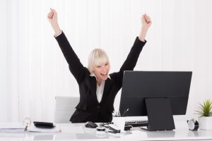 16945229-happy-businesswoman-raising-arms-at-desk